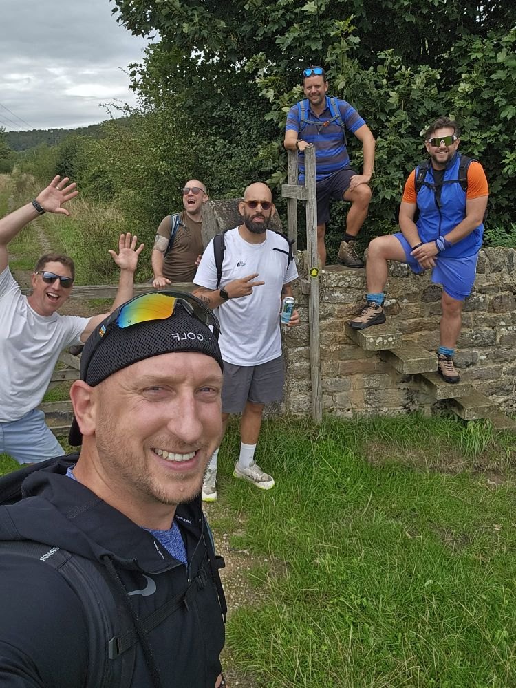A smiling group of hikers gathered at a stone stile