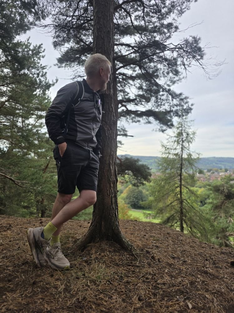 A hiker leaning on a pine tree above a green valley