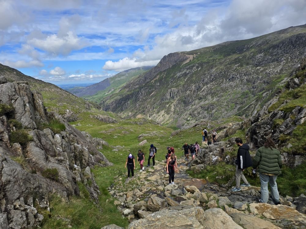 A line of hikers climbing through a rocky valley in Snowdonia