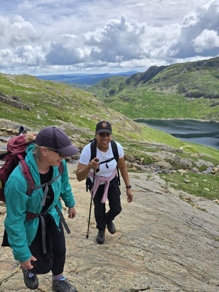 Hikers with poles walking up a rock slab above a lake