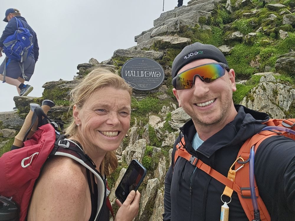Two hikers celebrating at the Snowdon summit marker