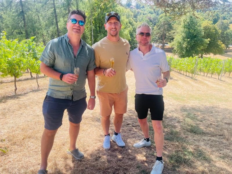 Three friends holding glasses of sparkling wine among the vines